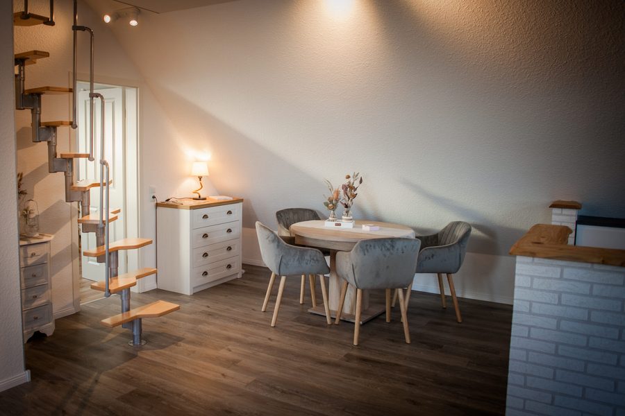 Wohn- und Essbereich der Ferienwohnung in Canhusen: heller Raum mit rundem Esstisch, vier Polsterstühlen und einer Wendeltreppe